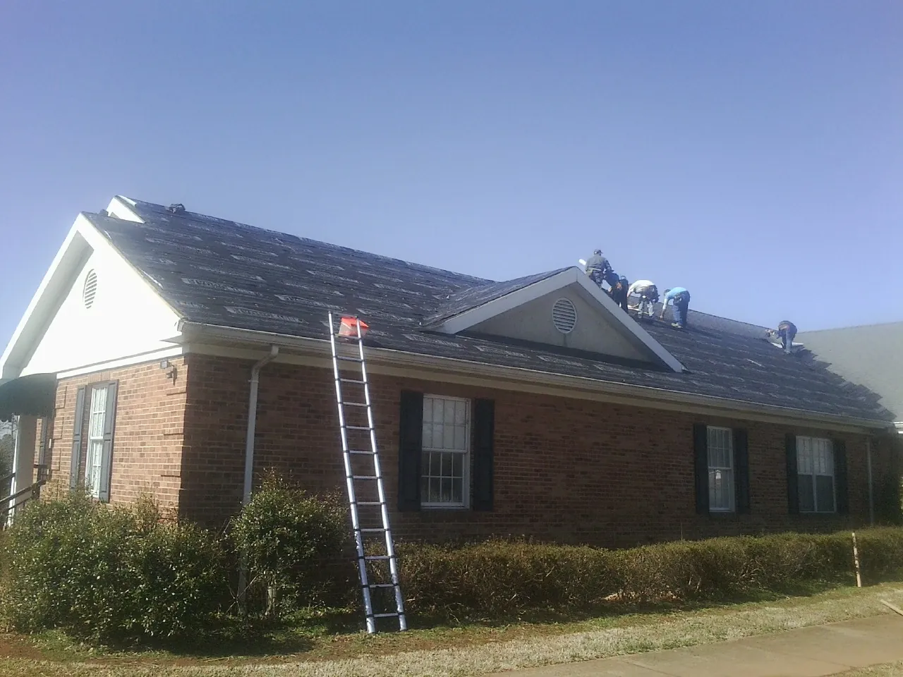 Crew tearing shingles off a brick ranch roof with a ladder set — Emergency Roof Repair work by our crew in Defiance